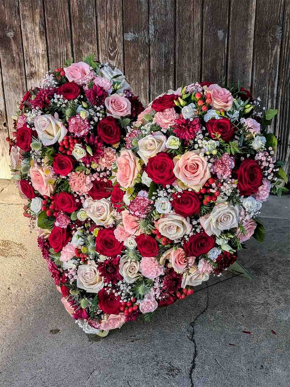 Ein Blumenkranz in Herzform aus verschiedenen Rosatönen und roten Rosen für eine Trauerfeier